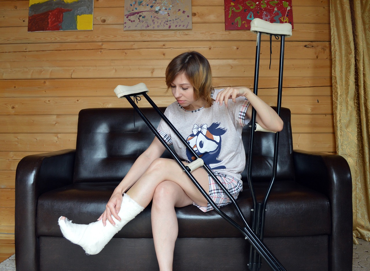 Women sitting on couch. Her left leg is in a cat and she has crutches leaning against her leg.
