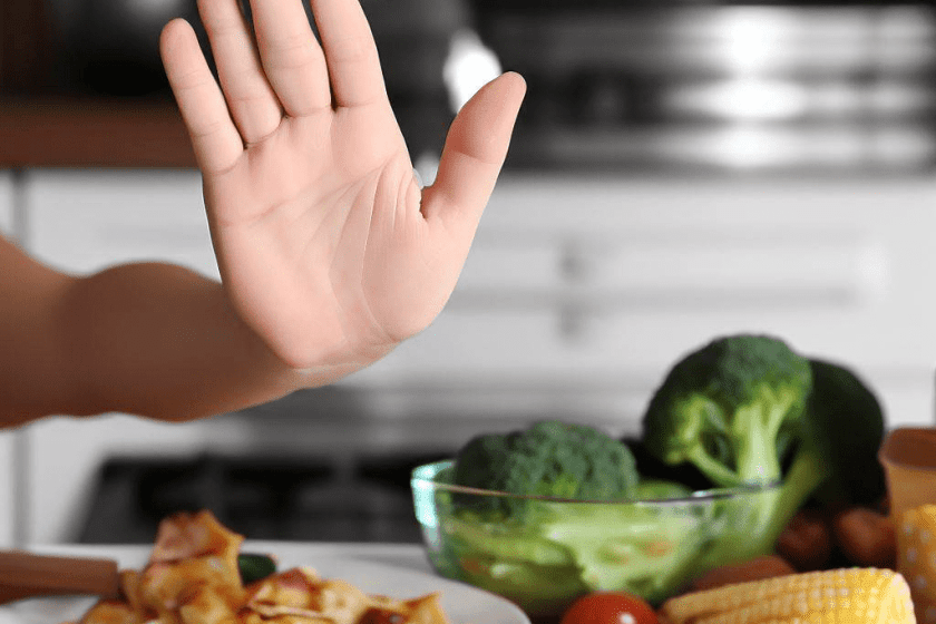 hand up saying no next to plate of food and vegetables.