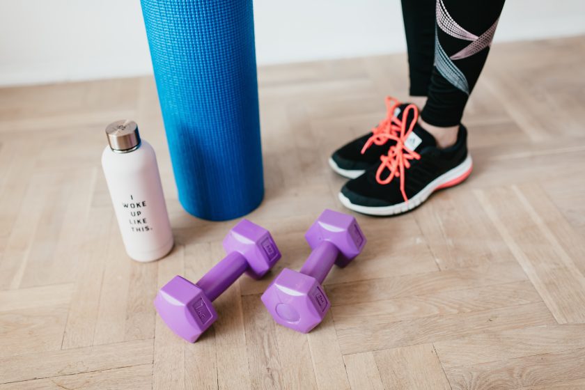Pilates mat, weights, bottle, person's feet with trainers on